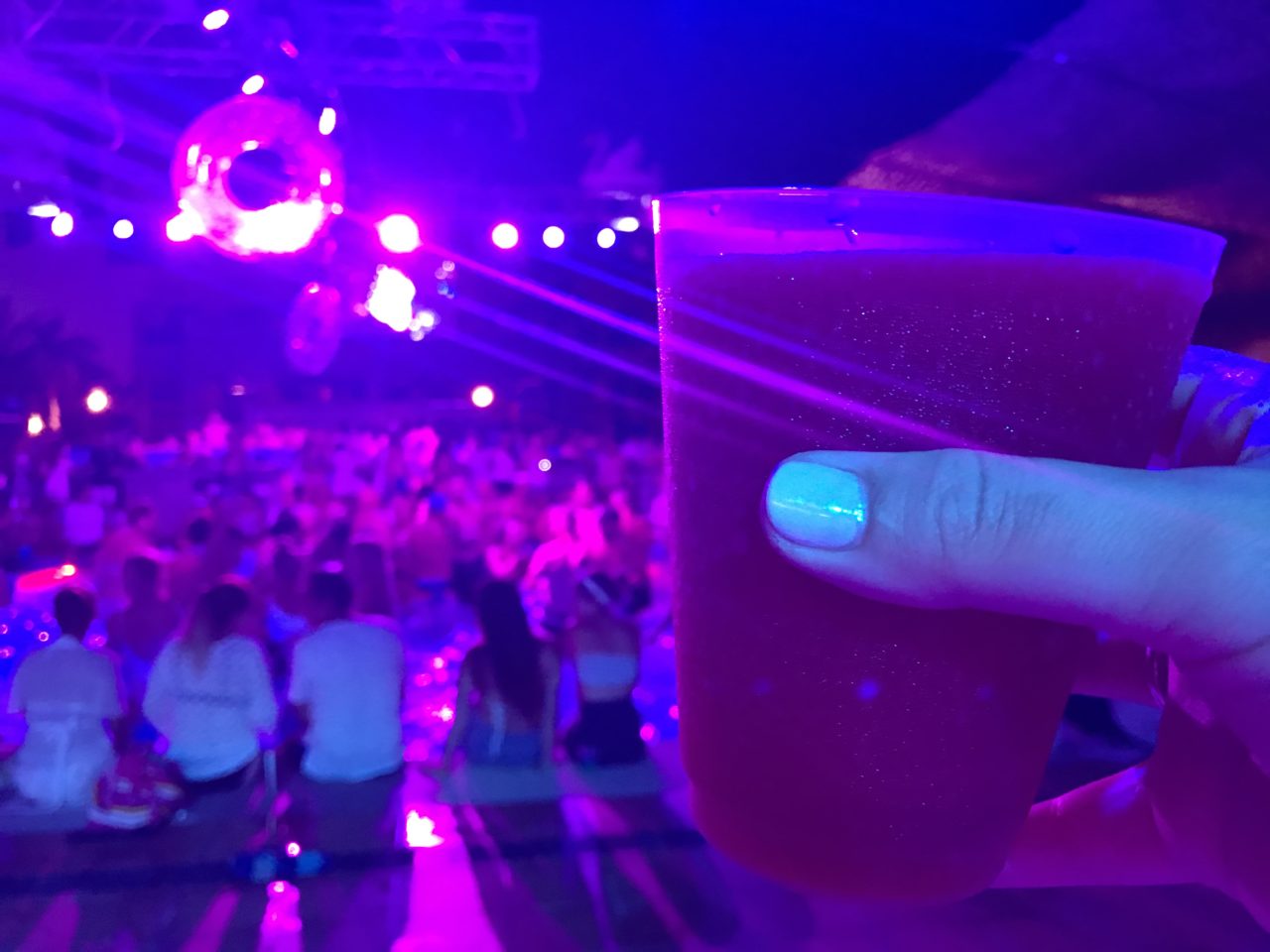 Drink in front of pool filled with dancing people