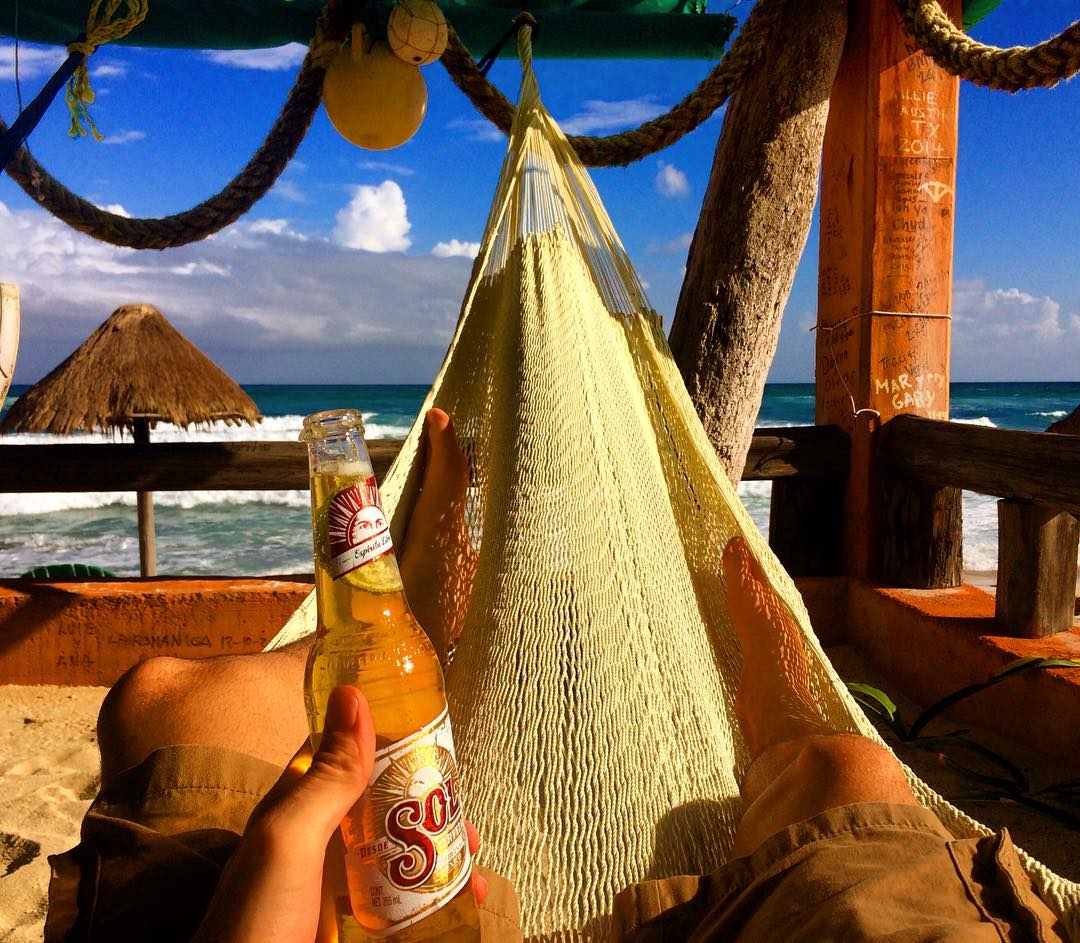 Person in hammock holding Sol beer with ocean in the background.