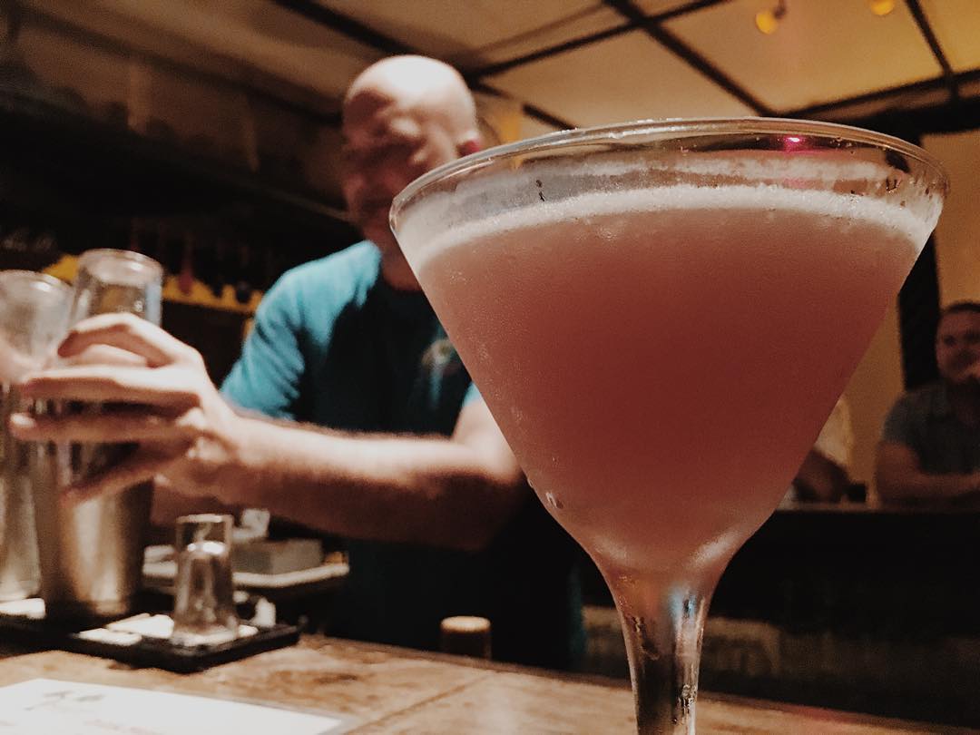 Martini on bar with bartender in background. 