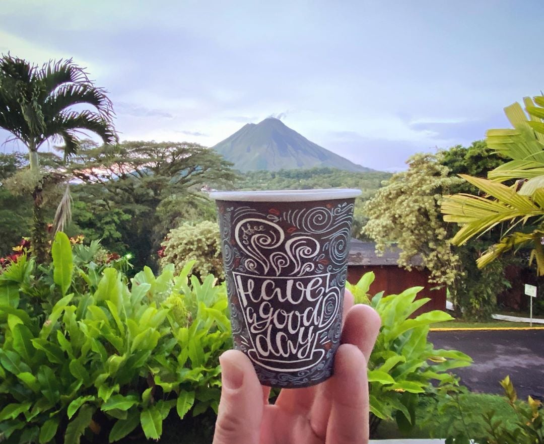 Someone holding coffee cup with volcano in the background.