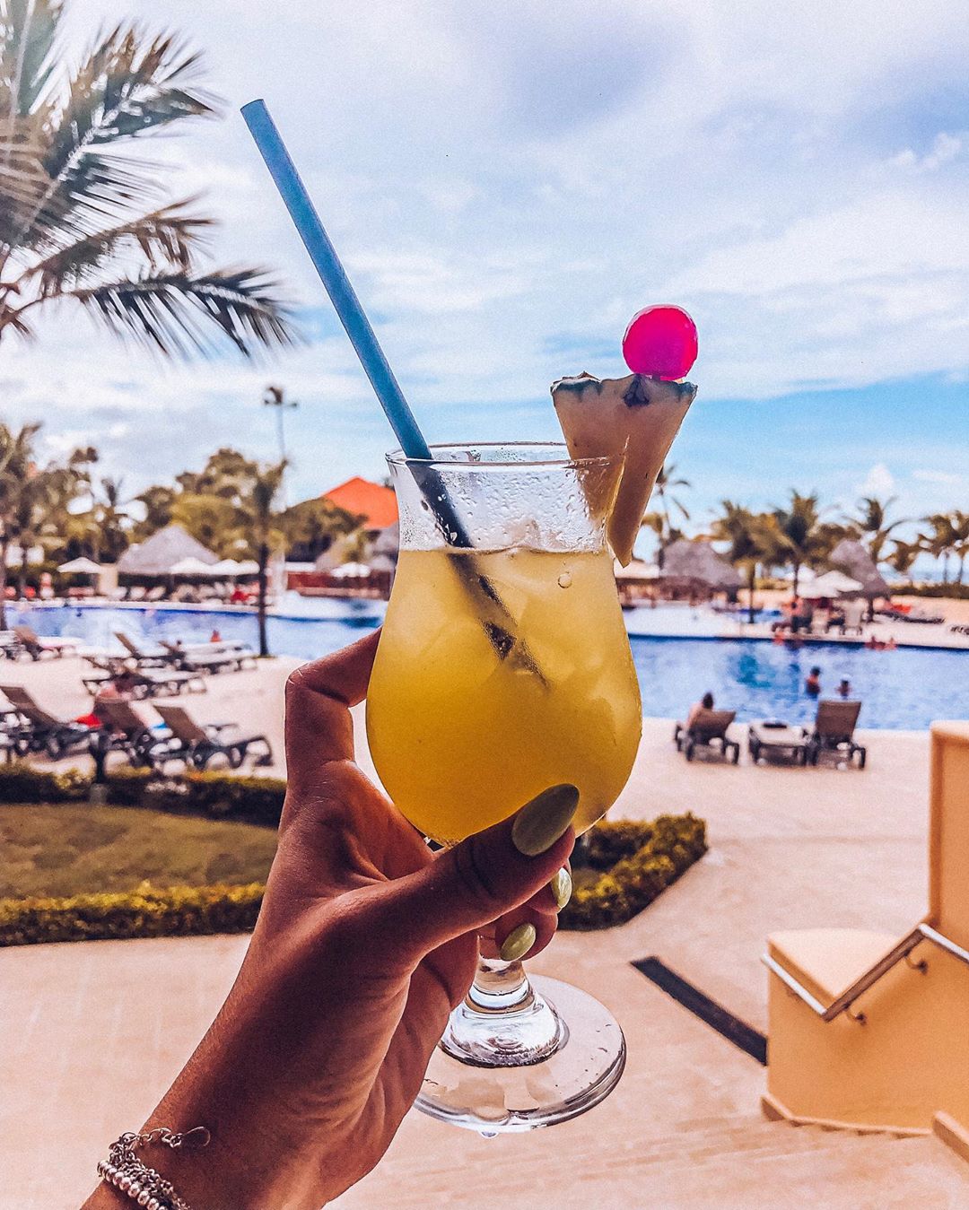 Girl holding pineapple drink with pool in background.