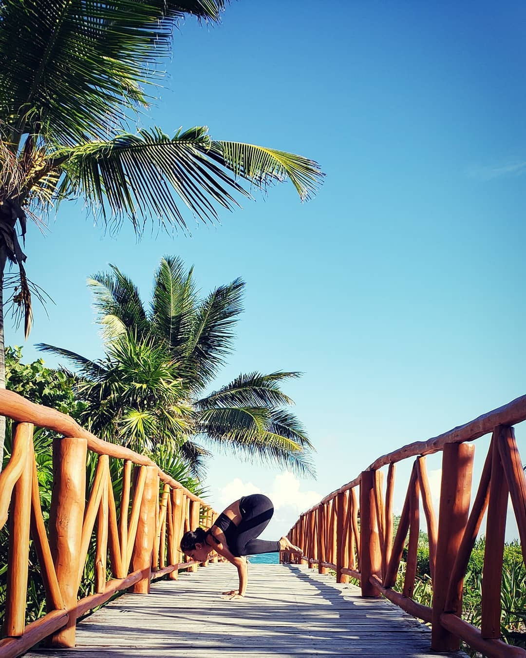 Girl doing yoga pose on walkway leading to beach. 