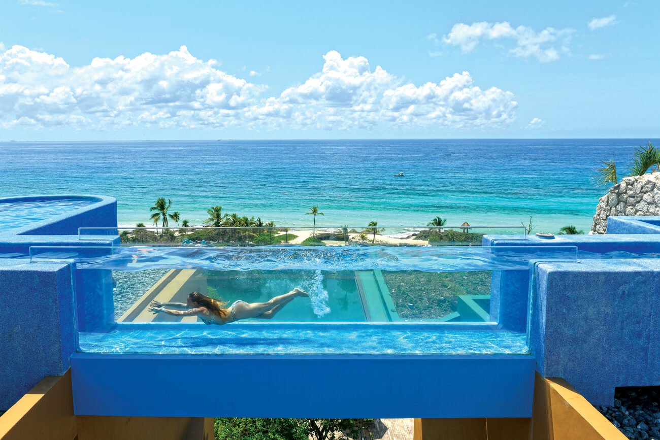 Girl swimming in transparent pool overlooking ocean.