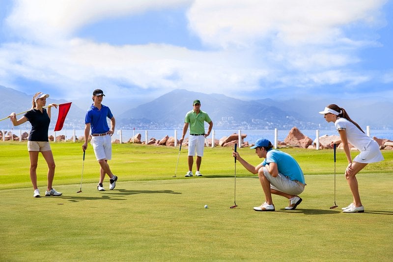 People on golf course with ocean and mountains in background.