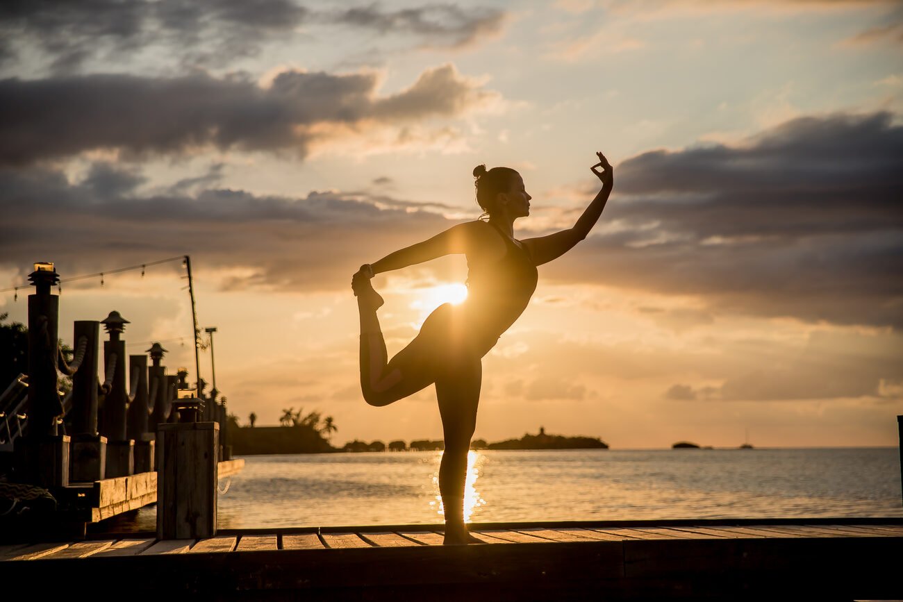 Girl doing sunrise yoga on dock over ocean.